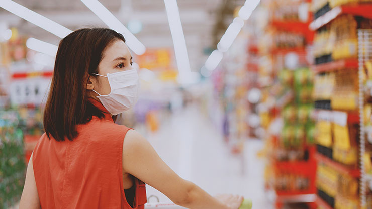 A young woman wearing a mask, shopping in a grocery store during the pandemic
